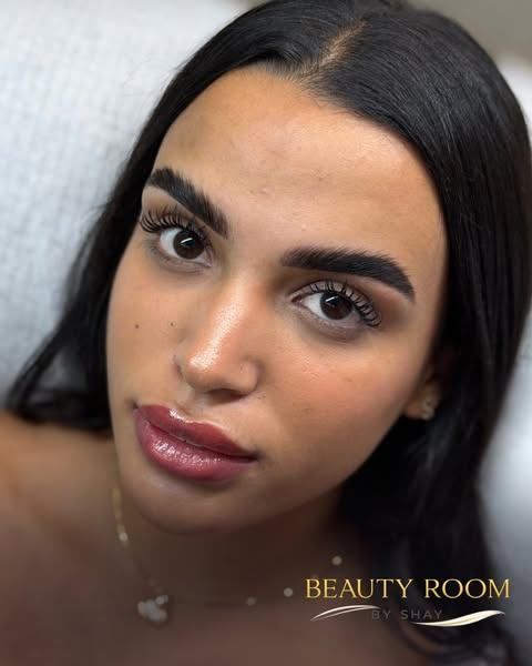 Primer plano de una mujer de cabello oscuro y labios brillantes, recostada sobre una almohada clara con expresión neutra.
