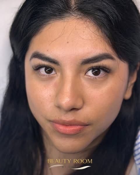 Retrato en primer plano de una persona con cabello oscuro y maquillaje natural, mirando al frente contra un fondo liso.