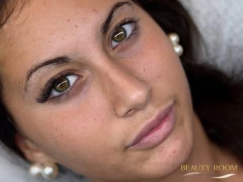 Retrato en primer plano de una mujer con cabello oscuro, pendientes de perlas y maquillaje suave, mirando a la cámara.