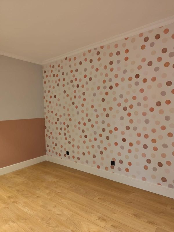 Habitación vacía con suelo de madera clara, papel pintado de lunares rosas y blancos y pared pintada en dos tonos.