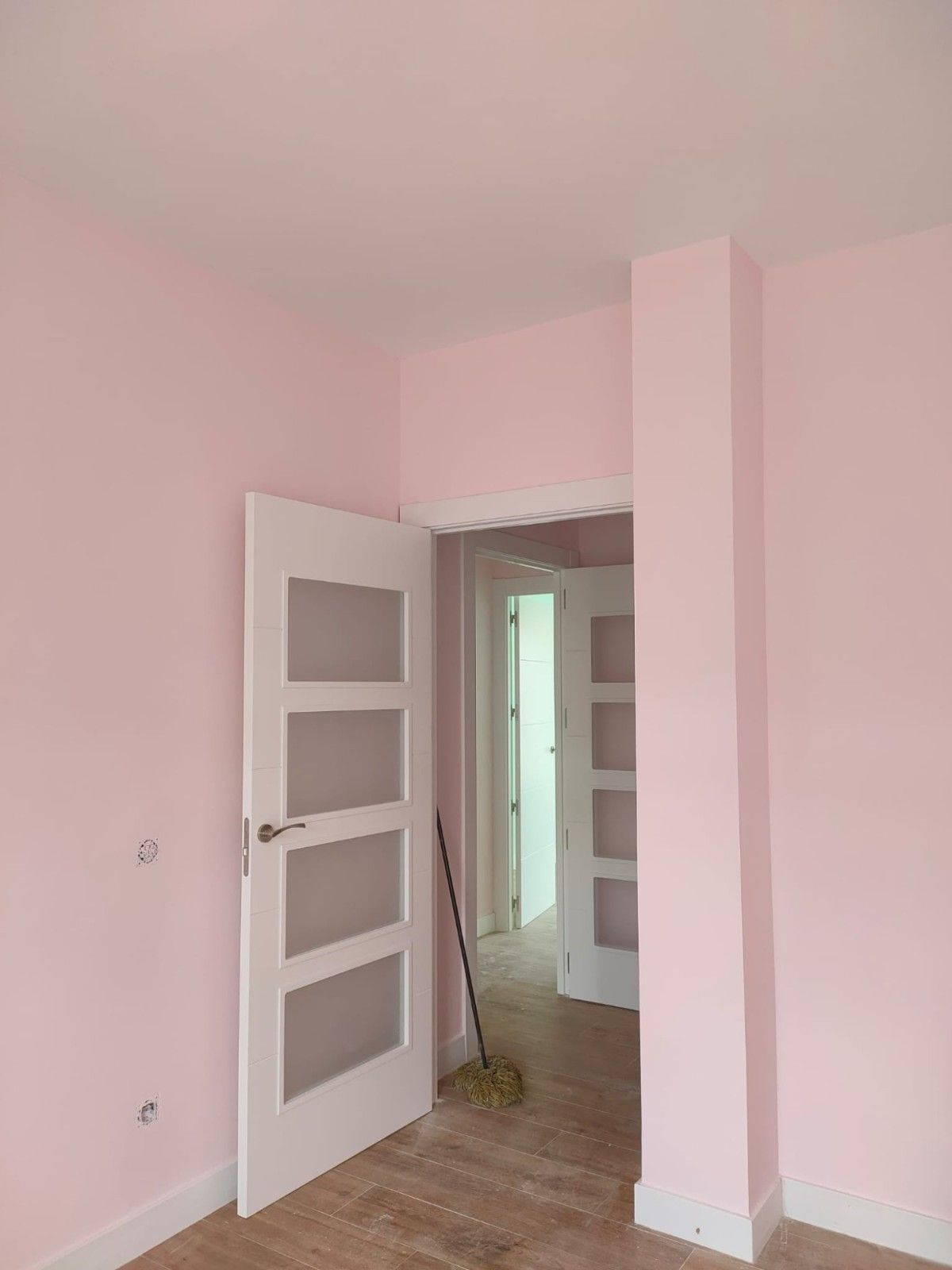 Habitación rosa con puerta blanca abierta y pasillo visible a través de ella.