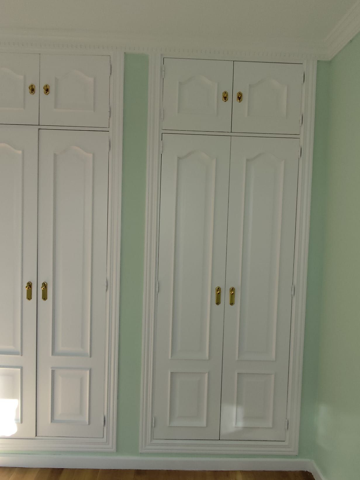 Armarios blancos con tiradores dorados montados sobre una pared de color verde pálido.