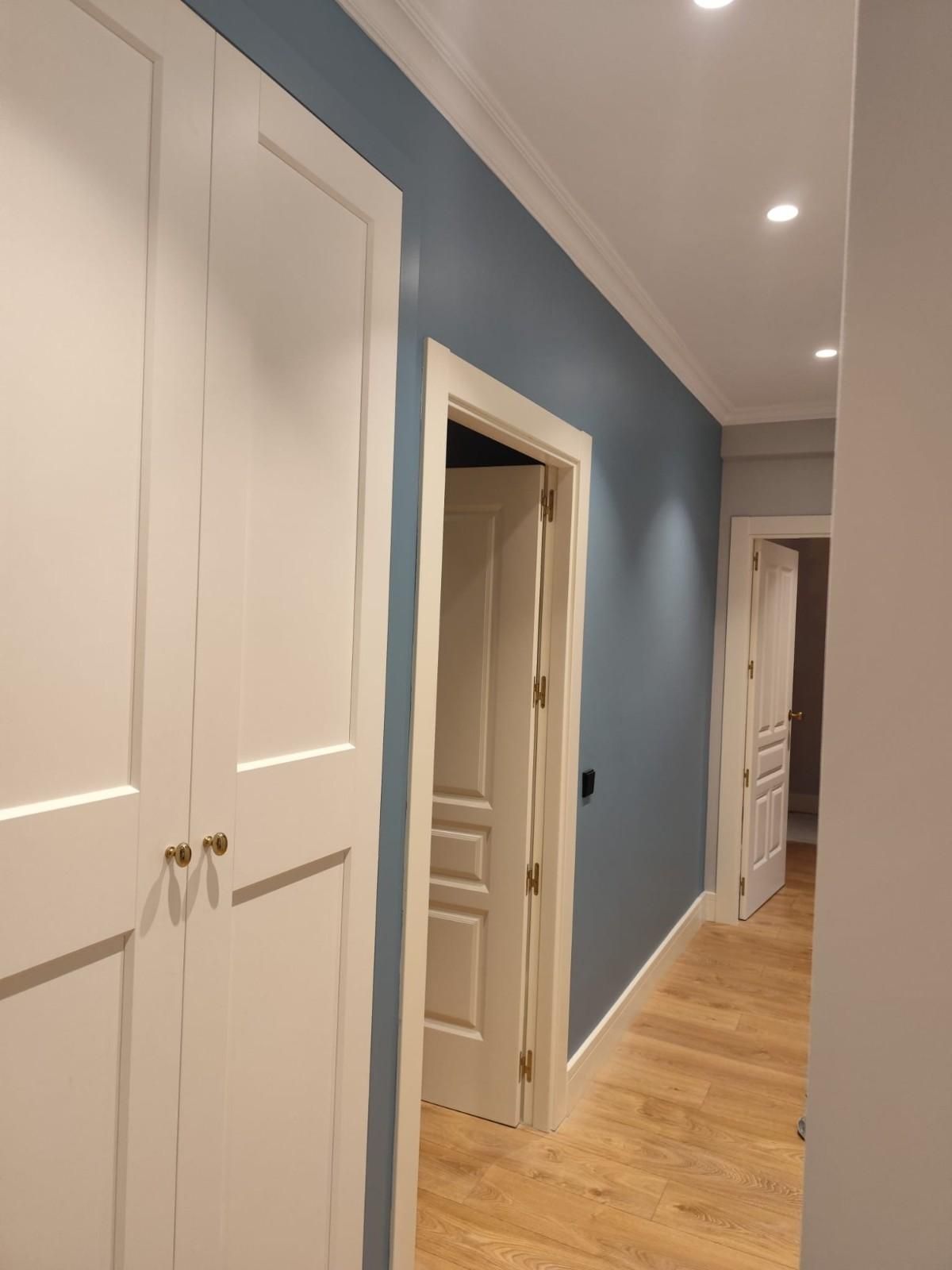 Pasillo con pared decorativa azul, puertas blancas y suelo de madera clara.