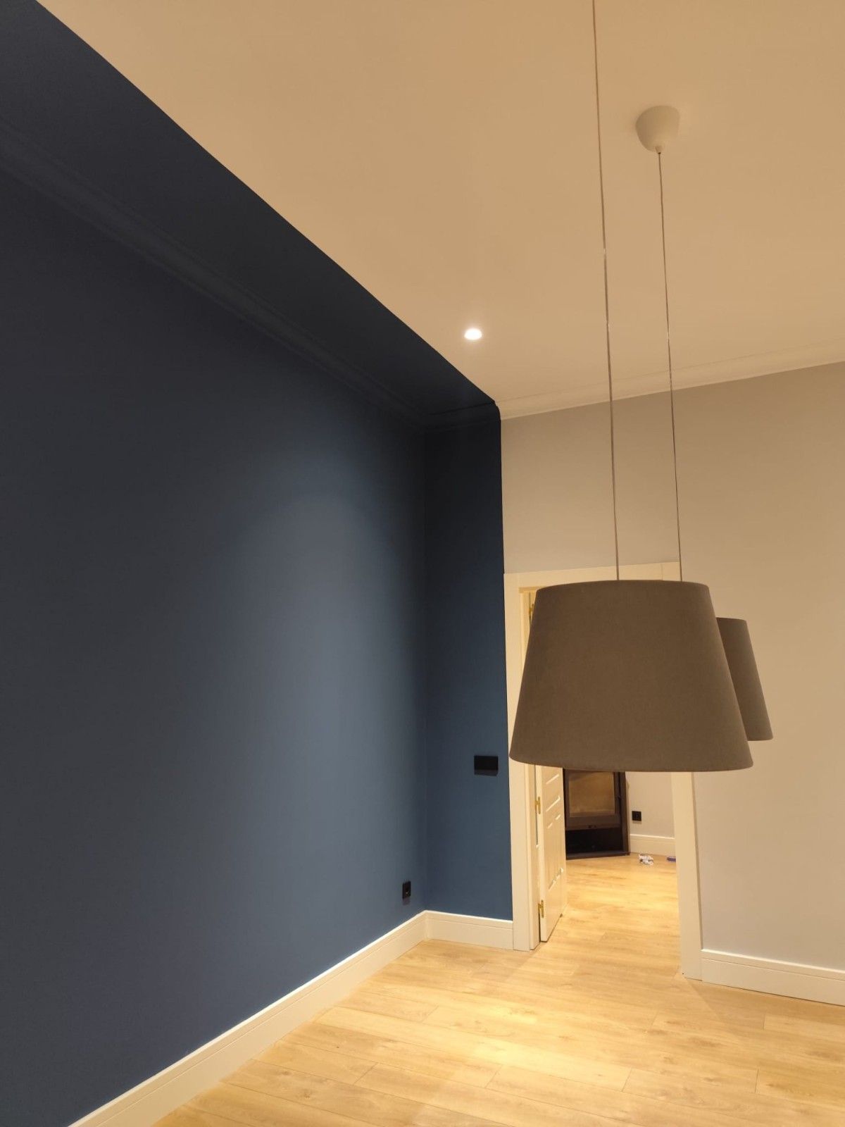 Habitación moderna con pared decorativa azul marino, suelo de madera clara y lámpara colgante.