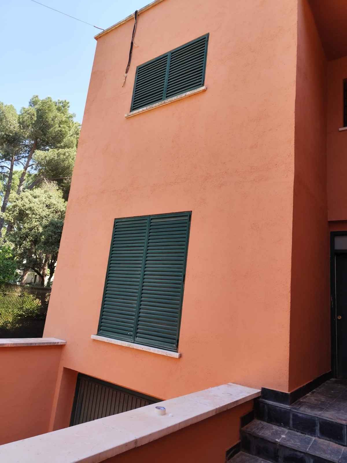 Edificio de estuco naranja con contraventanas verdes y barandilla de escalera en el exterior.