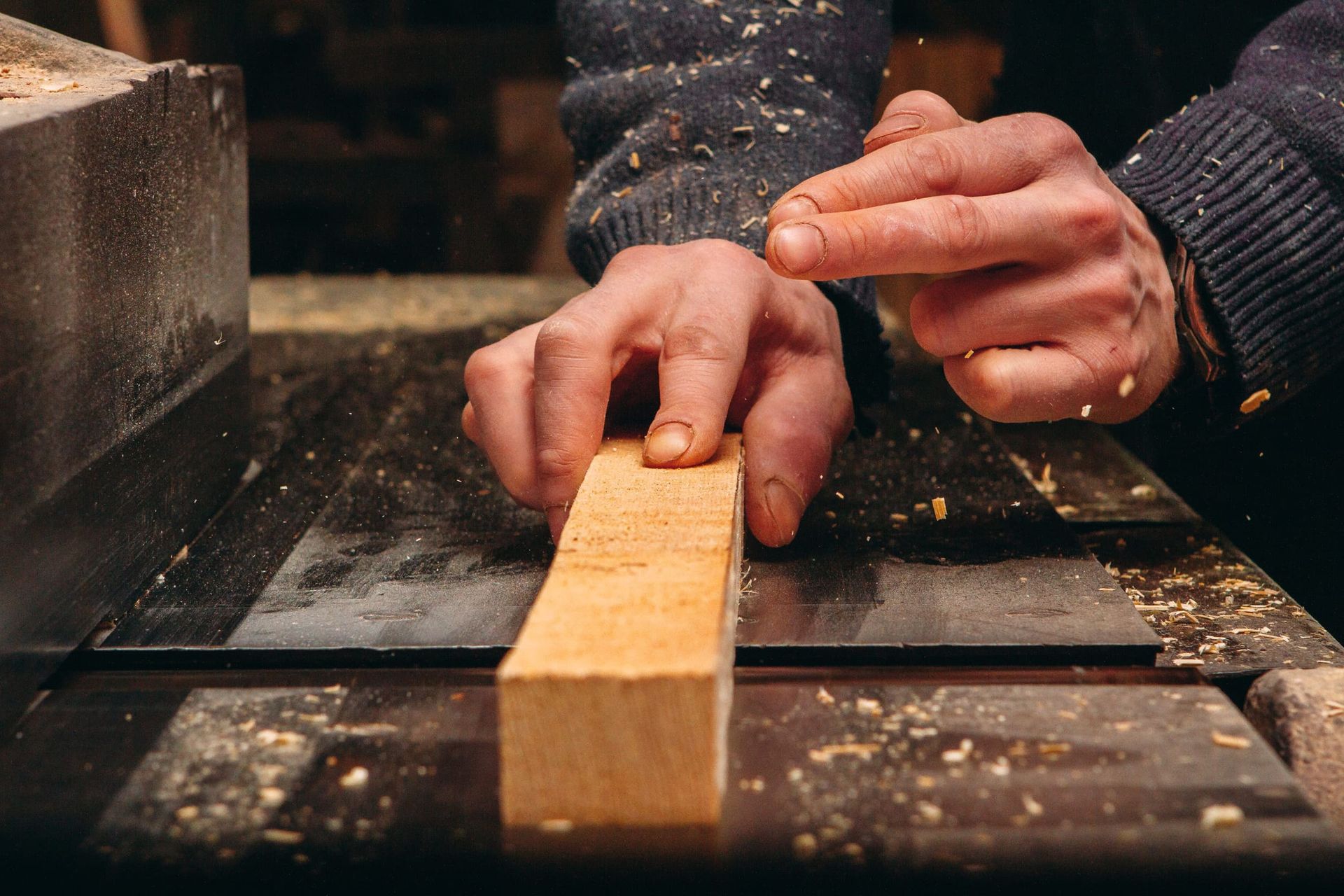 Primer plano de unas manos guiando un pequeño bloque de madera sobre la superficie de una sierra de mesa en un taller.