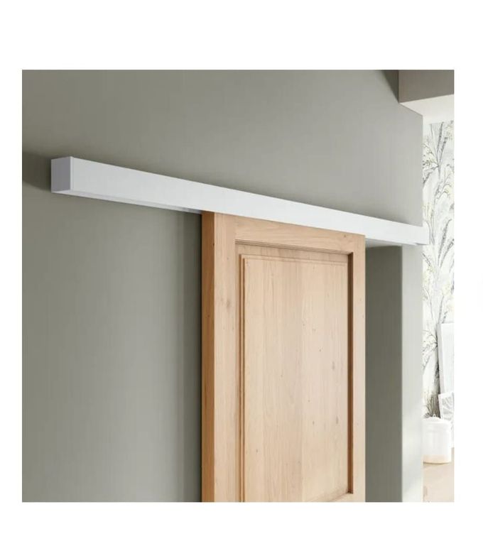 Una puerta corredera de madera montada sobre un sistema de rieles blancos contra una pared gris claro.