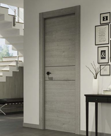 Una puerta interior de madera gris con tirador negro, situada junto a una escalera y un cuadro enmarcado en la pared.