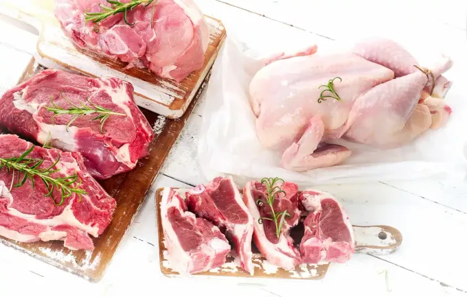 Carnes crudas variadas: cerdo, chuletas de cordero y un pollo entero dispuestos en tablas de cortar.