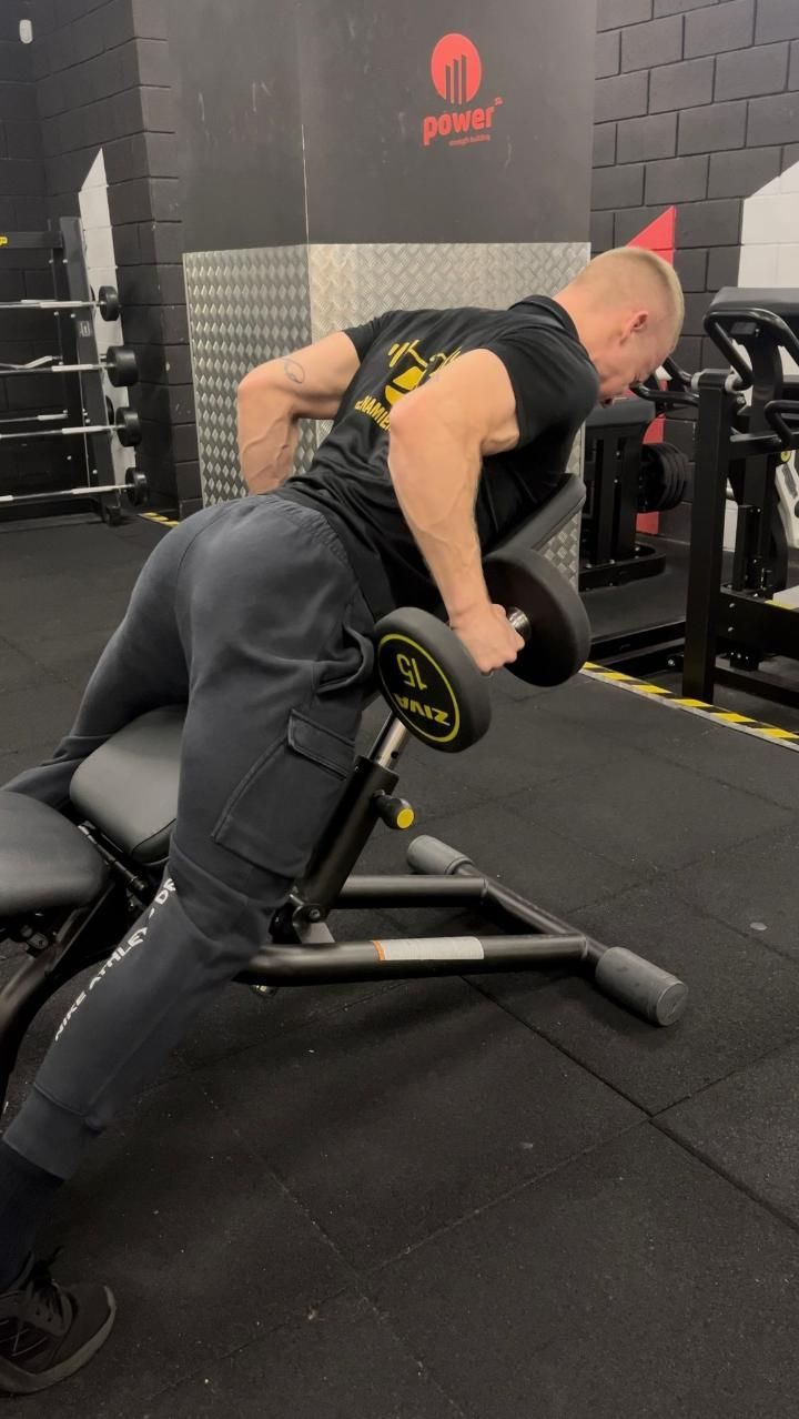 Hombre realizando una fila inclinada con mancuernas en un banco inclinado en un gimnasio.
