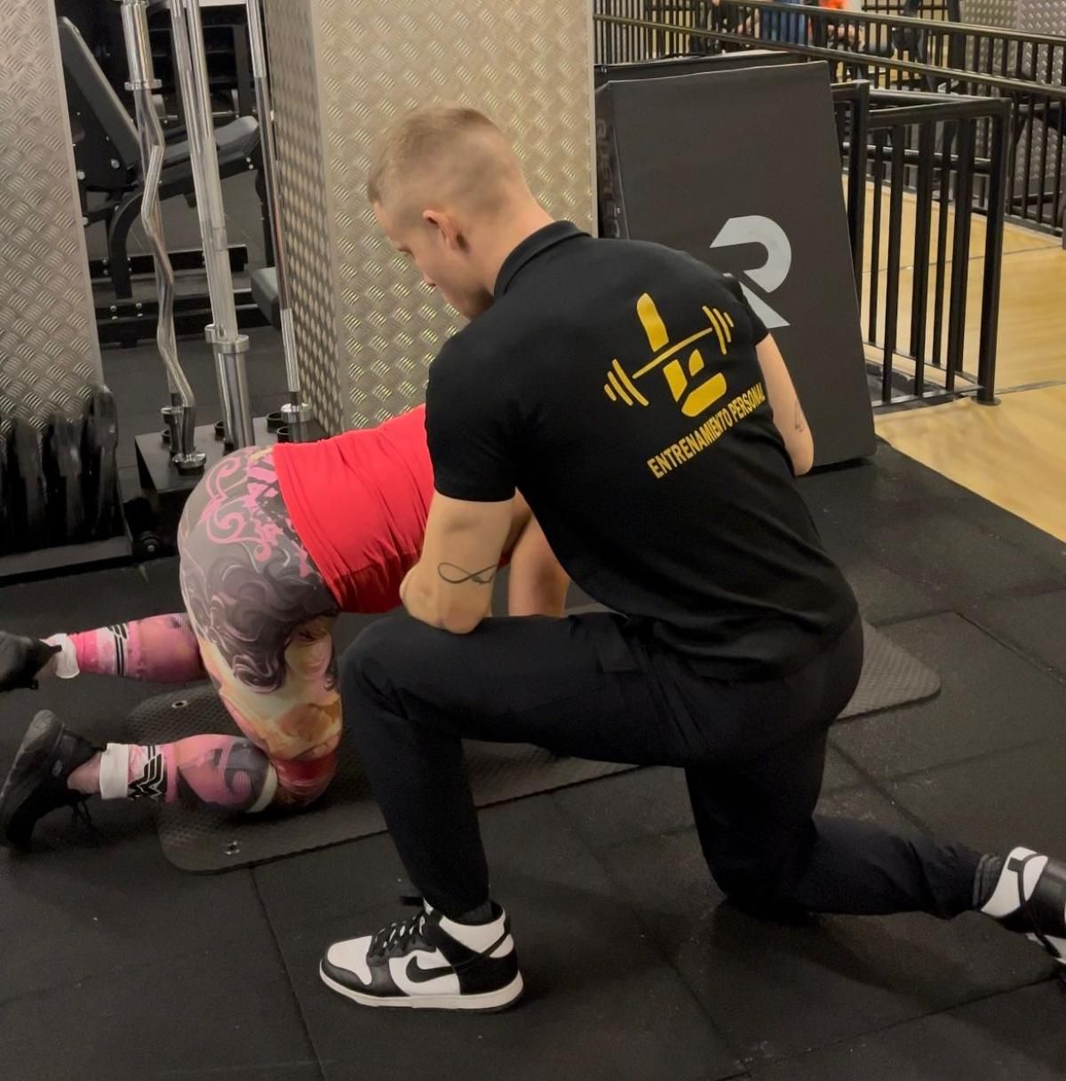 Una persona que hace ejercicio sobre una colchoneta recibe la ayuda de un entrenador en un gimnasio.