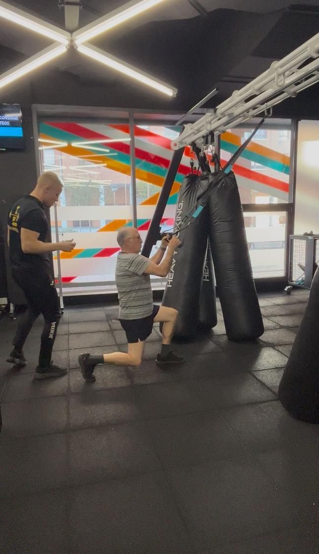 Hombre arrodillado, tirando de un entrenador de suspensión con la ayuda del entrenador en un gimnasio.