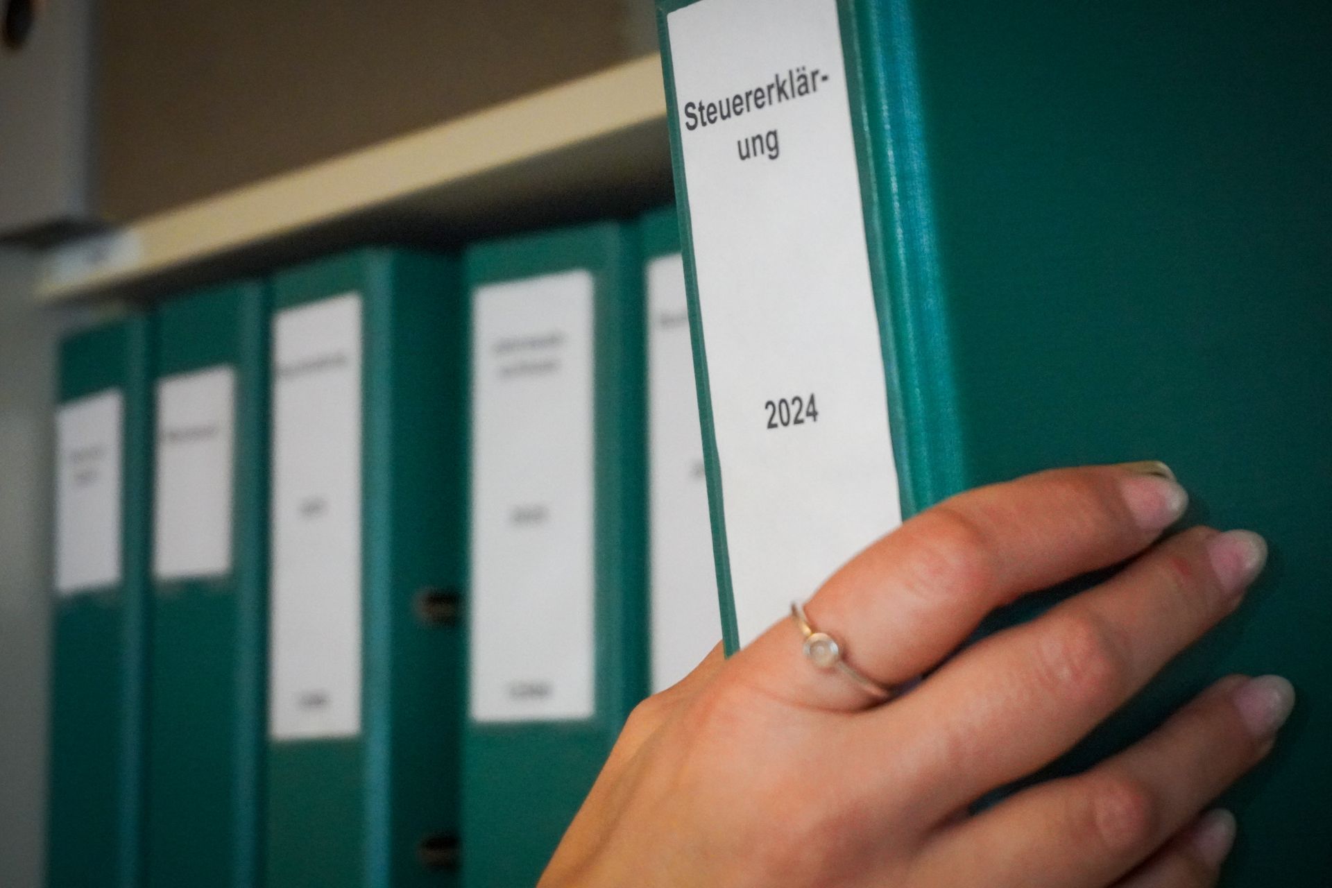 Ich wähle von Hand einen roten Ordner mit der Aufschrift „Steuer“ (Steuern) aus einer Reihe schwarzer Ordner aus.