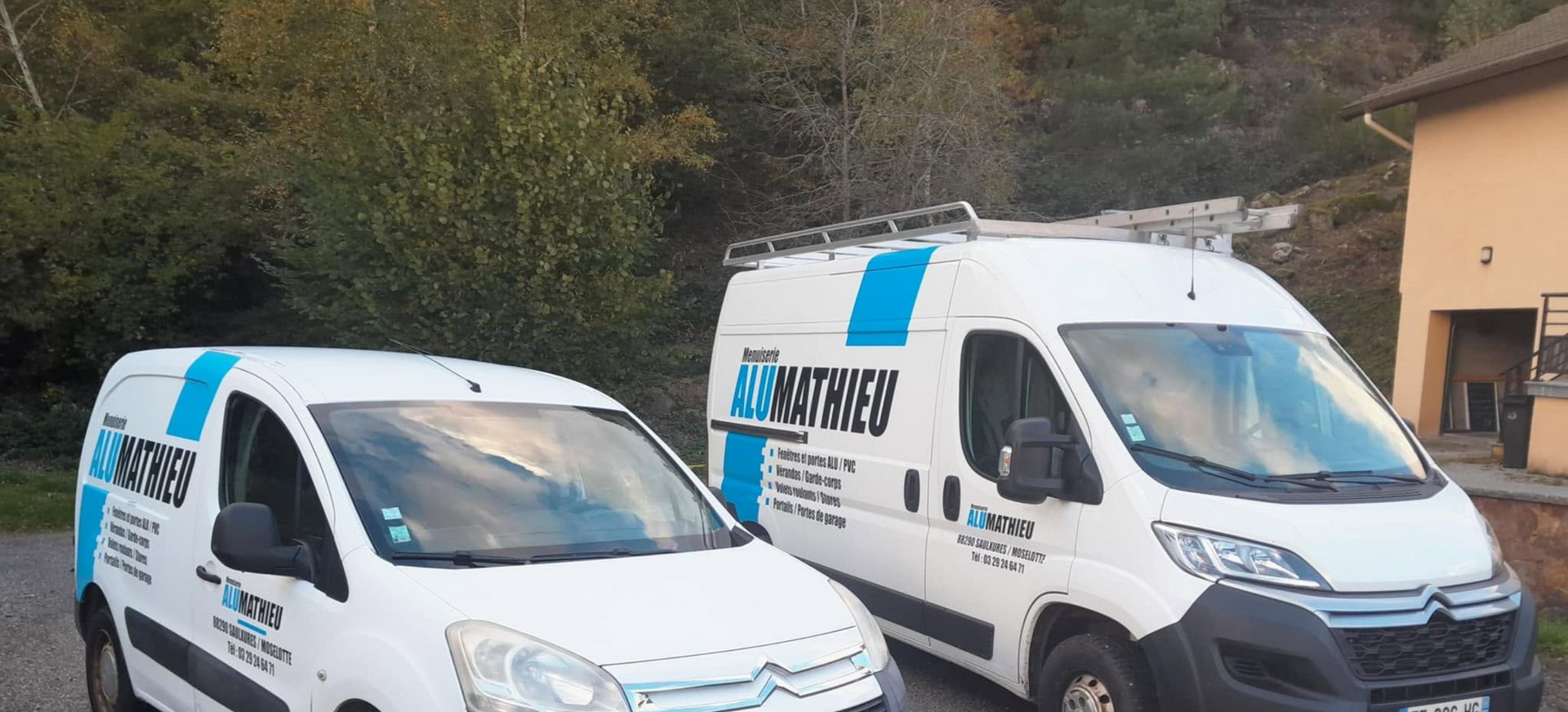 Deux fourgonnettes de service blanches avec des logos bleus étaient garées en bord de route.