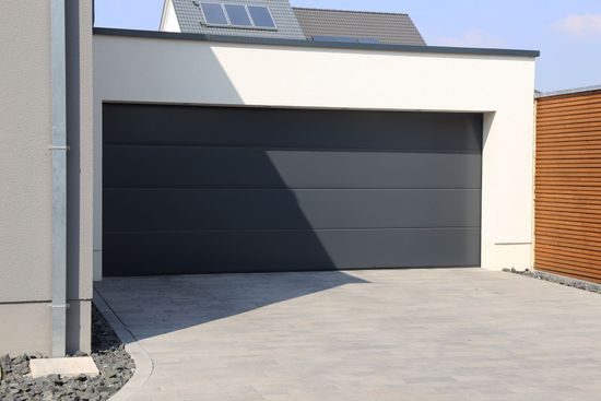 Maison moderne avec une porte de garage sombre et fermée et une allée en béton.