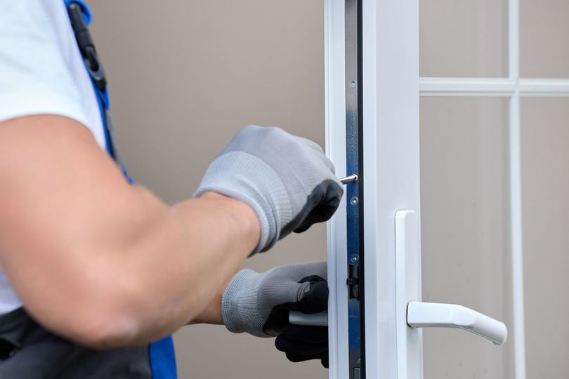 Un ouvrier ganté installe une poignée de porte blanche sur une porte.