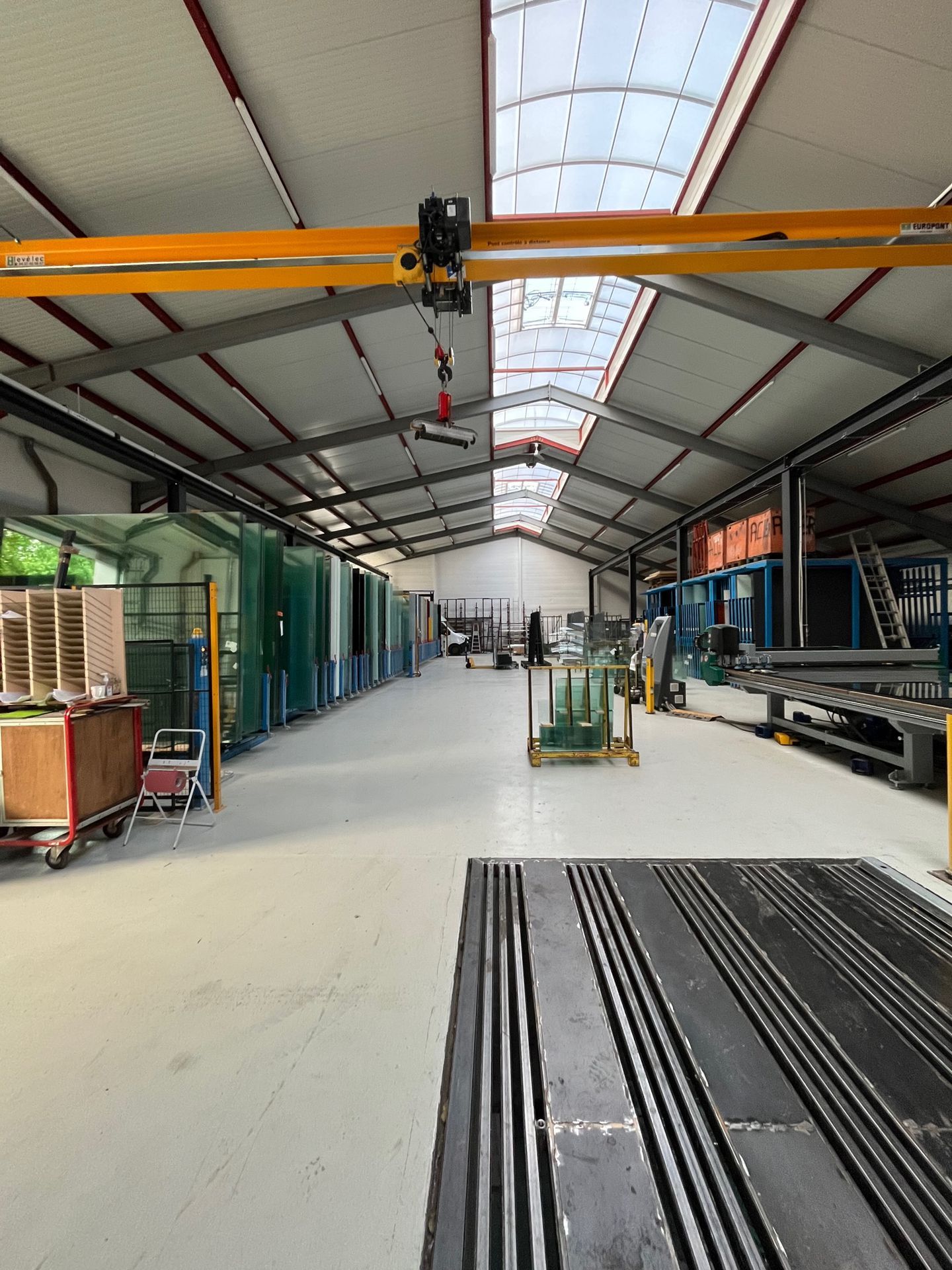 Intérieur d'un entrepôt industriel avec pont roulant, puits de lumière et panneaux de verre.