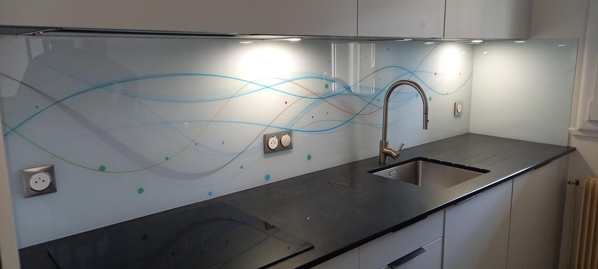 Cuisine avec plan de travail noir, crédence en verre à motif bleu et robinet en acier inoxydable.