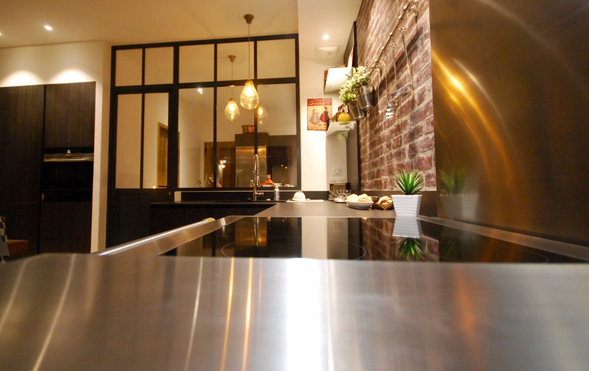 Cuisine moderne avec comptoir en acier inoxydable, mur en briques et cloison vitrée.
