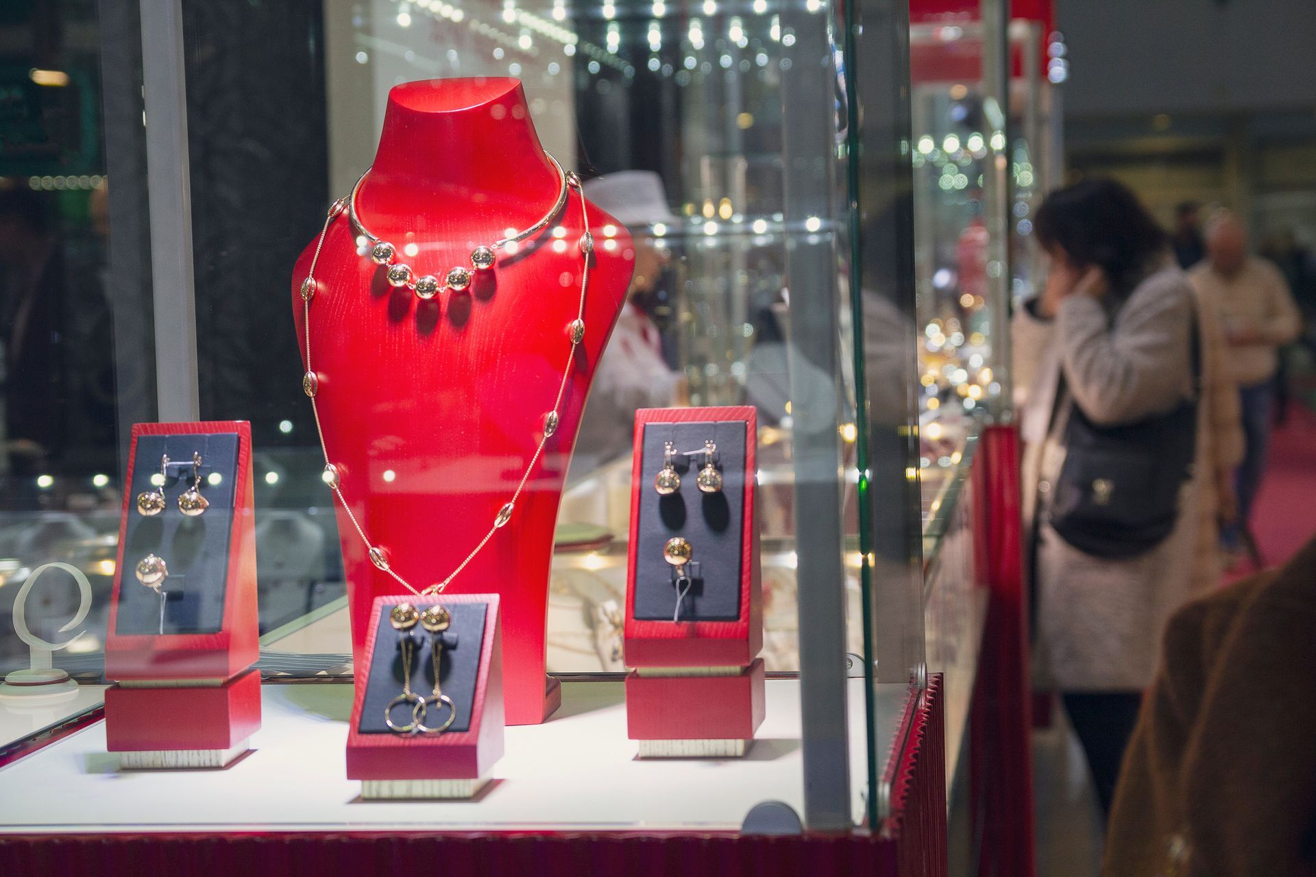 Vitrine à bijoux avec collier et boucles d'oreilles sur des supports en velours rouge ; une personne regarde la vitrine.