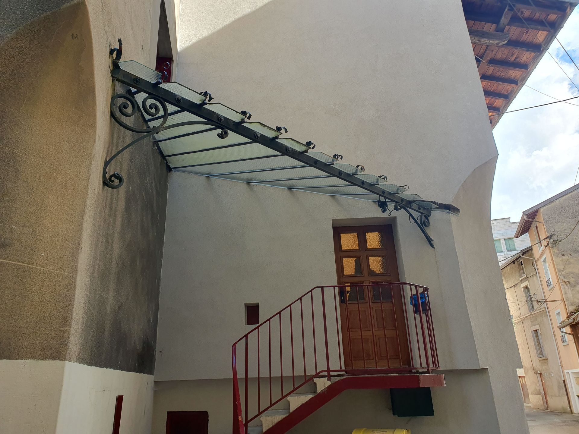 Vue extérieure d'un bâtiment avec une porte rouge, un escalier en métal et un auvent en verre orné.