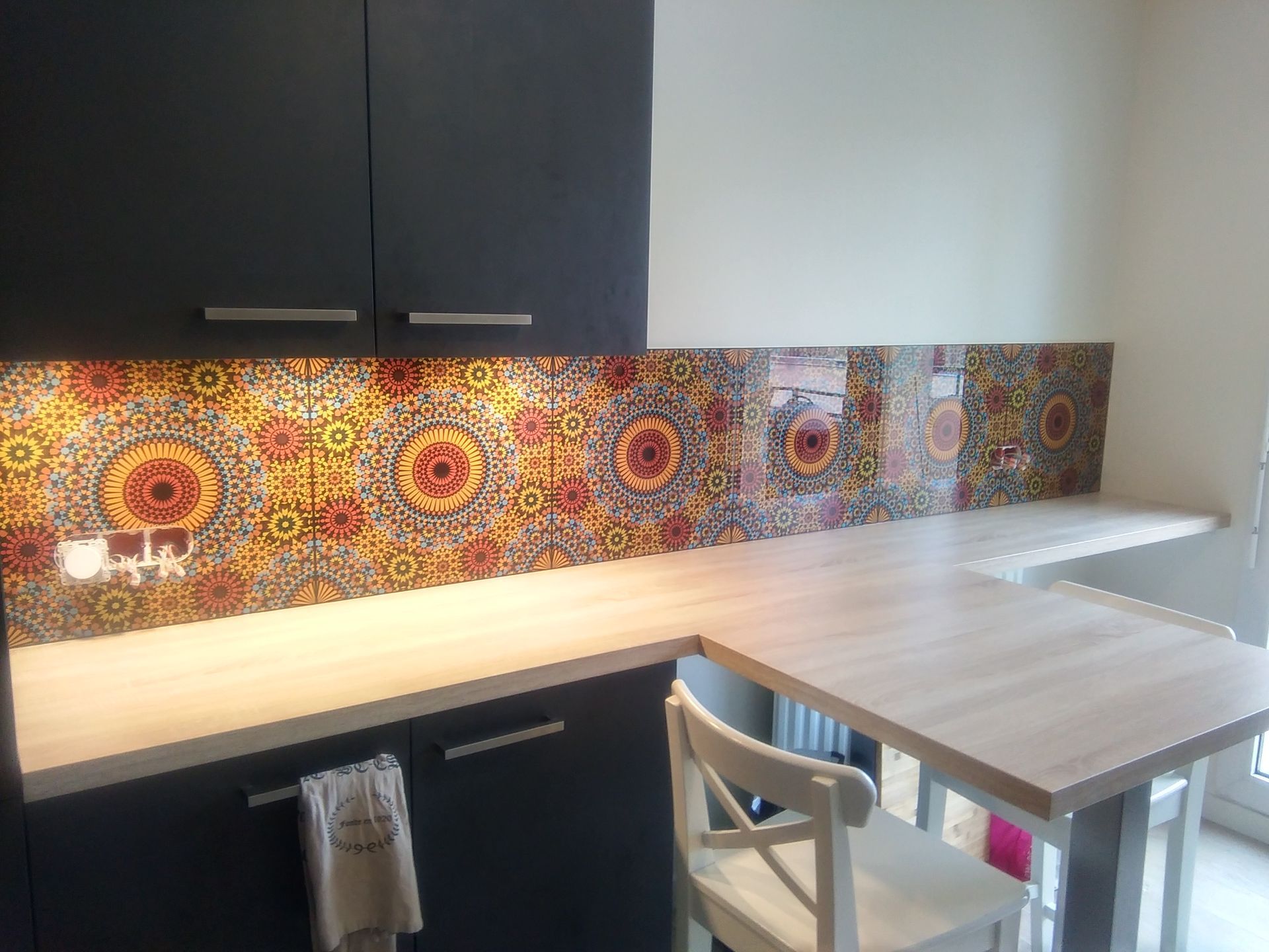Un coin cuisine avec des placards gris foncé, un plan de travail en bois clair et une crédence décorative aux couleurs vives de style marocain.