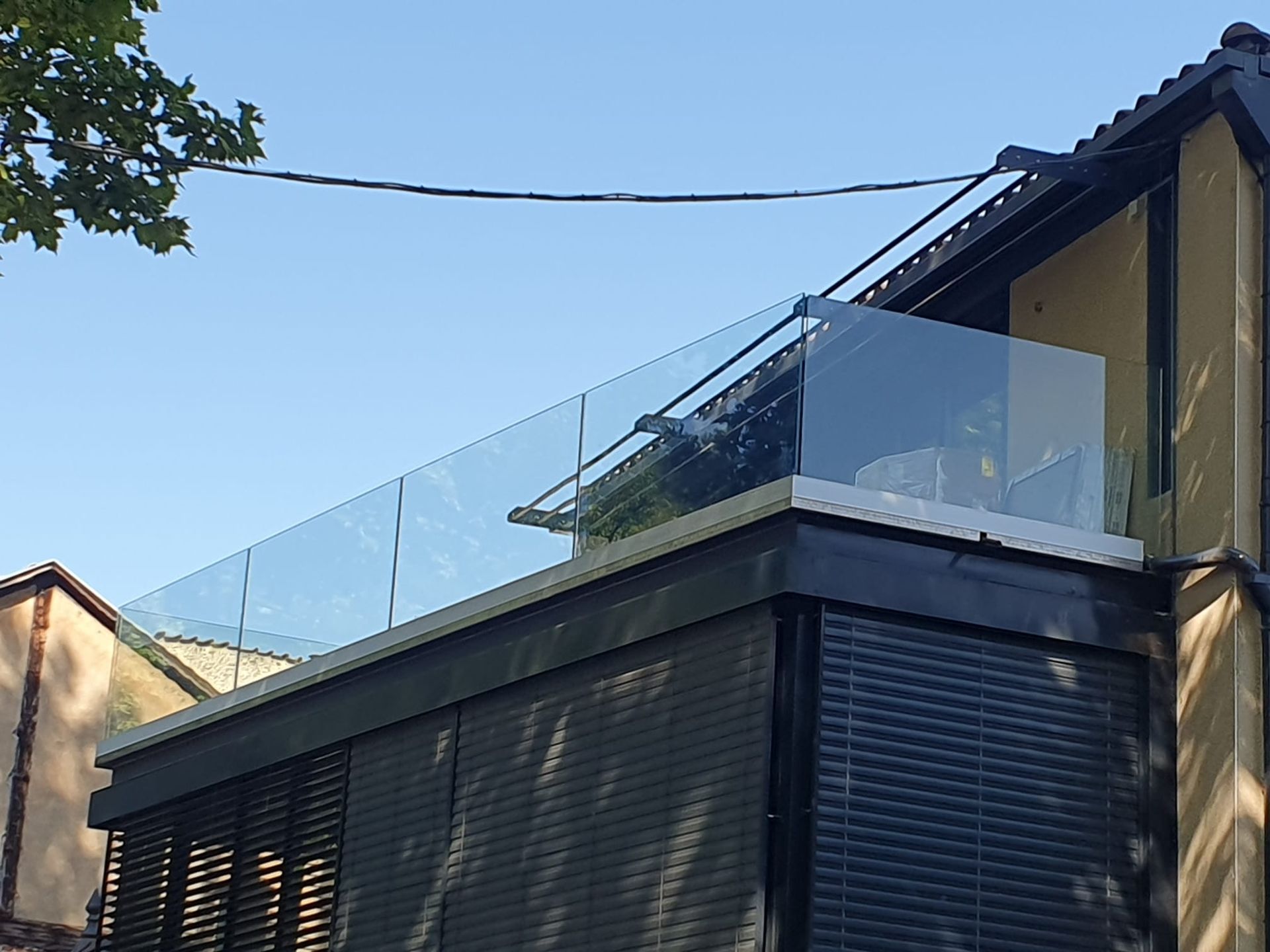 Balcon à balustrade vitrée sur un immeuble aux volets sombres. Journée ensoleillée, ciel dégagé.