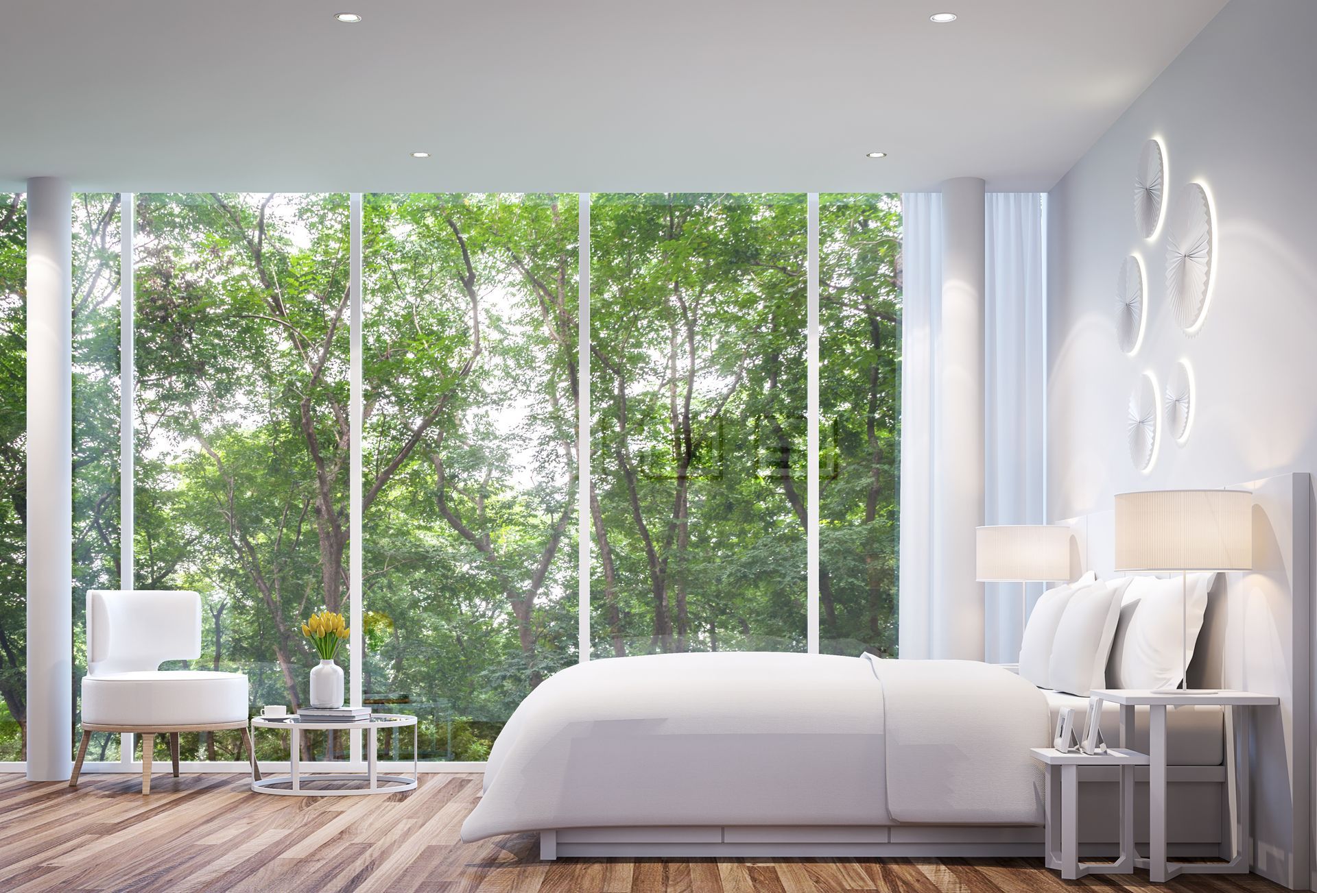 Chambre blanche avec grande fenêtre donnant sur des arbres verdoyants. Lit, chaise, tables de chevet.