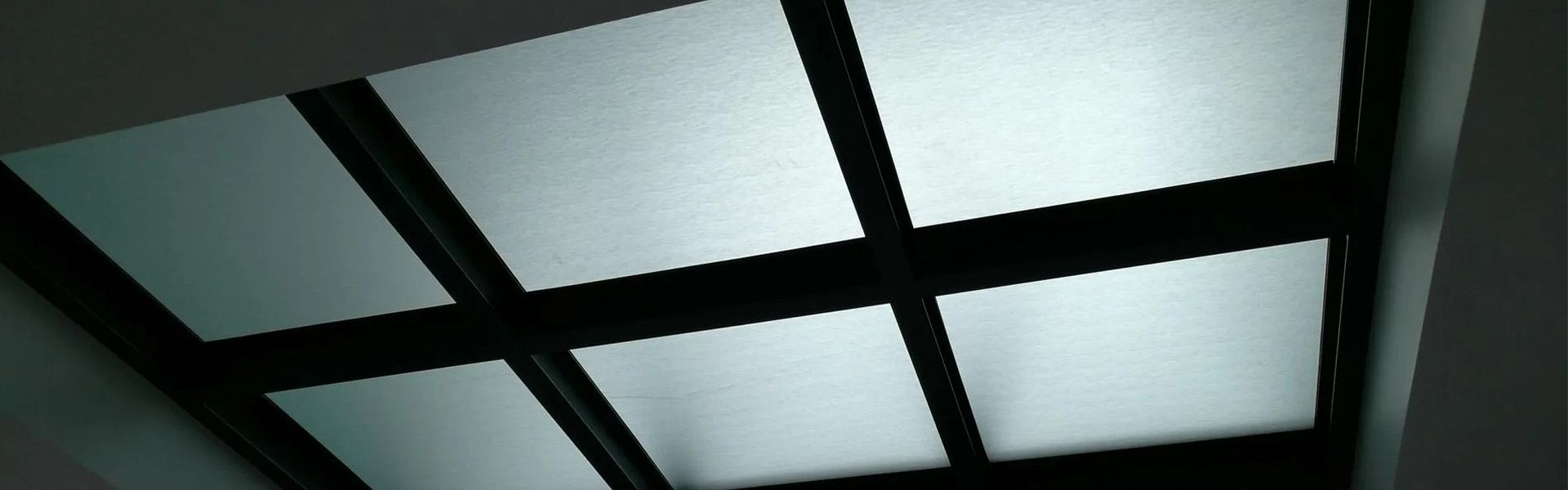 Plafond composé de panneaux carrés illuminés, séparés par des poutres noires.
