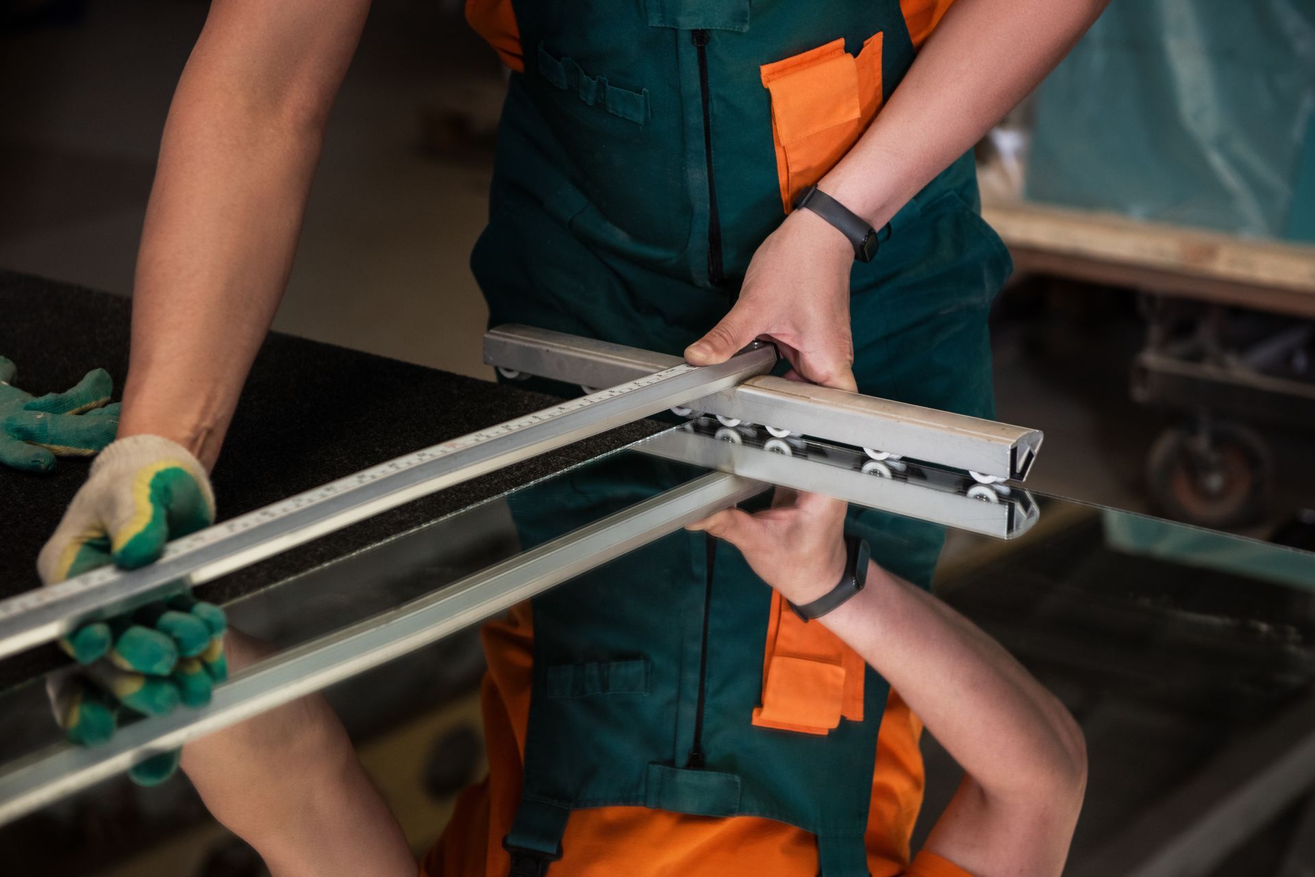 Un ouvrier en salopette verte et gants assemble un cadre métallique sur une table d'usine.