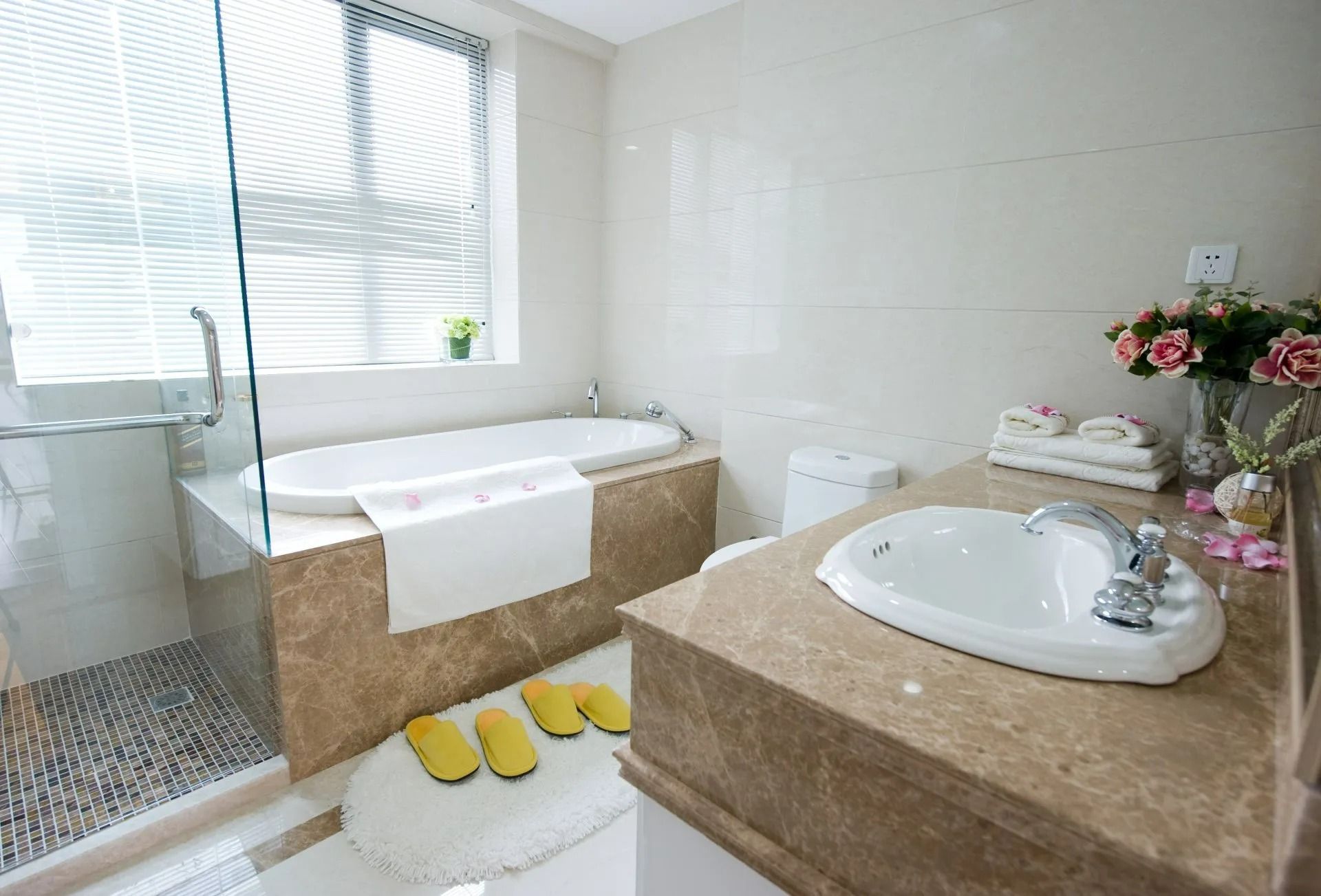 Salle de bains moderne avec baignoire ovale, comptoirs en marbre et fenêtre avec stores.