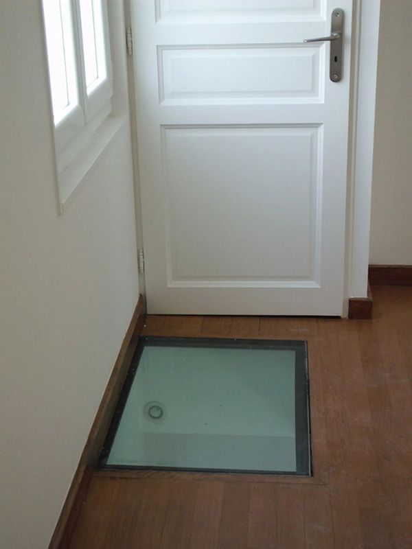 Un panneau de verre encastré dans un plancher en bois, devant une porte blanche fermée.