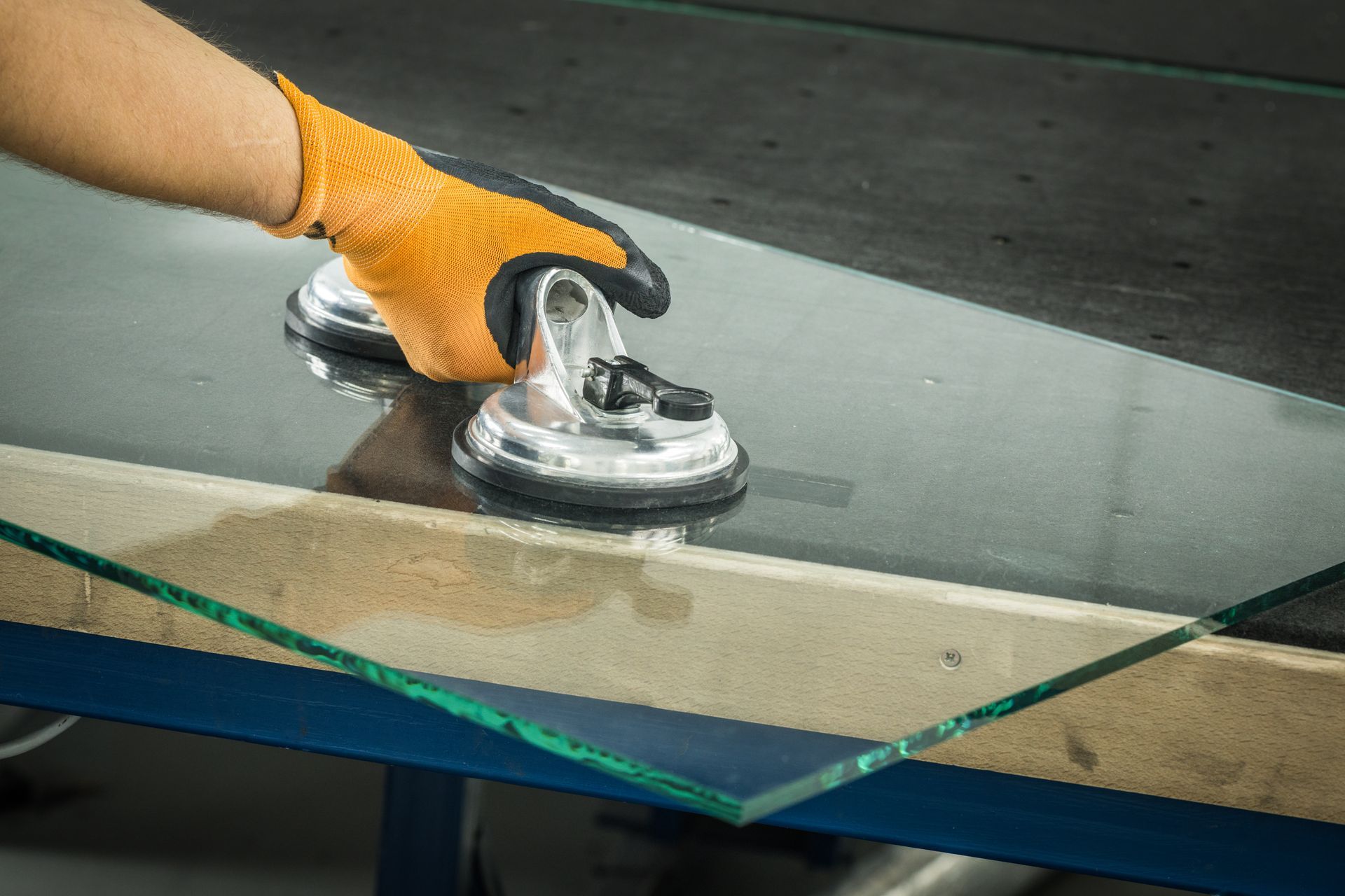 Main gantée d'orange utilisant une ventouse pour soulever une plaque de verre d'une surface en bois.