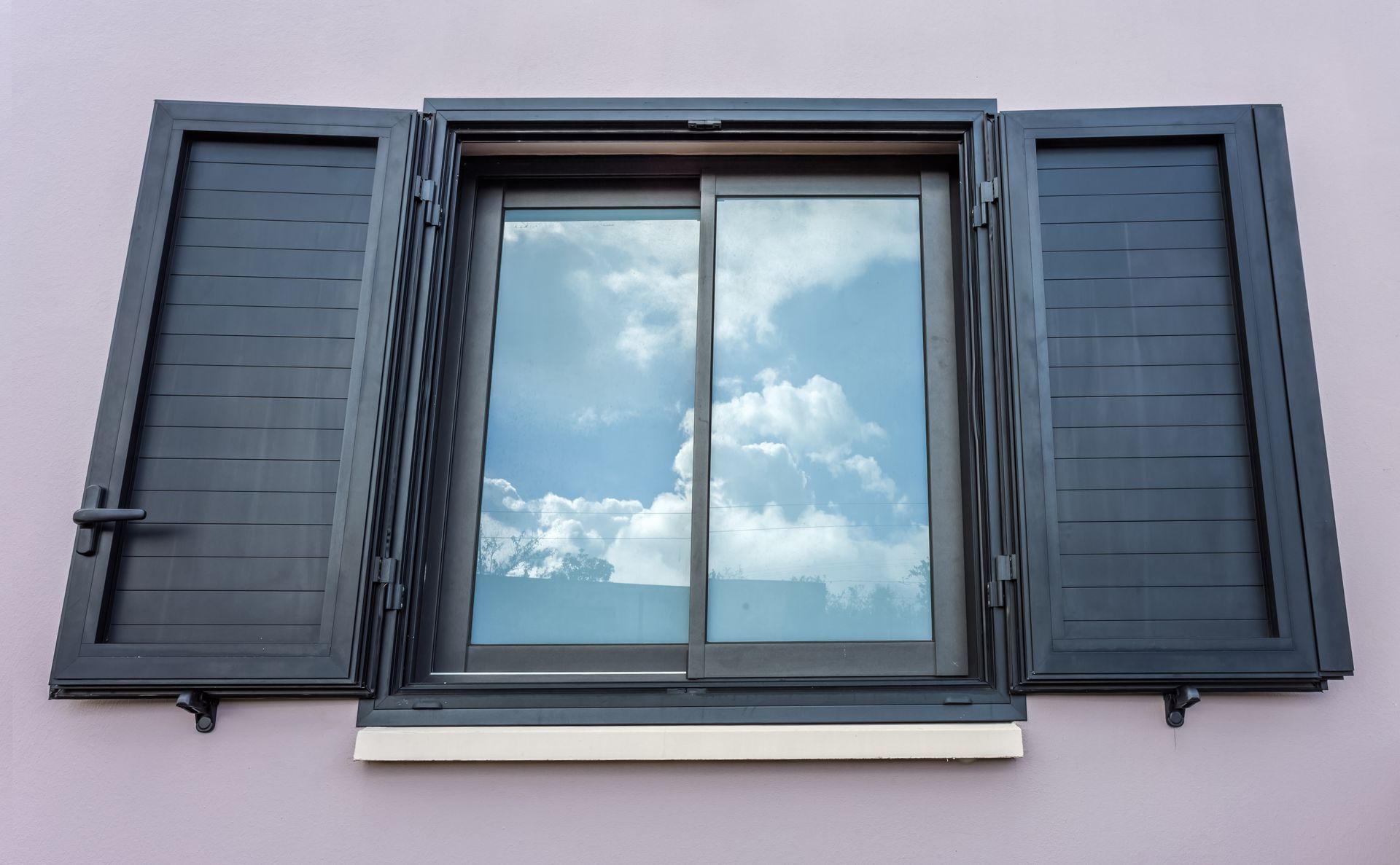 Fenêtre aux volets sombres ouverts, reflétant un ciel nuageux.