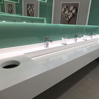 Un baño con un lavabo largo, grifos y un espejo.