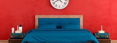 Hay un reloj en la pared encima de la cama en el dormitorio.