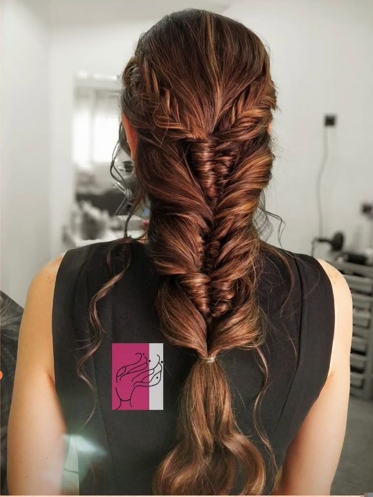 Mujer con un peinado oscuro y trenzado desde atrás. Top negro y fondo neutro.