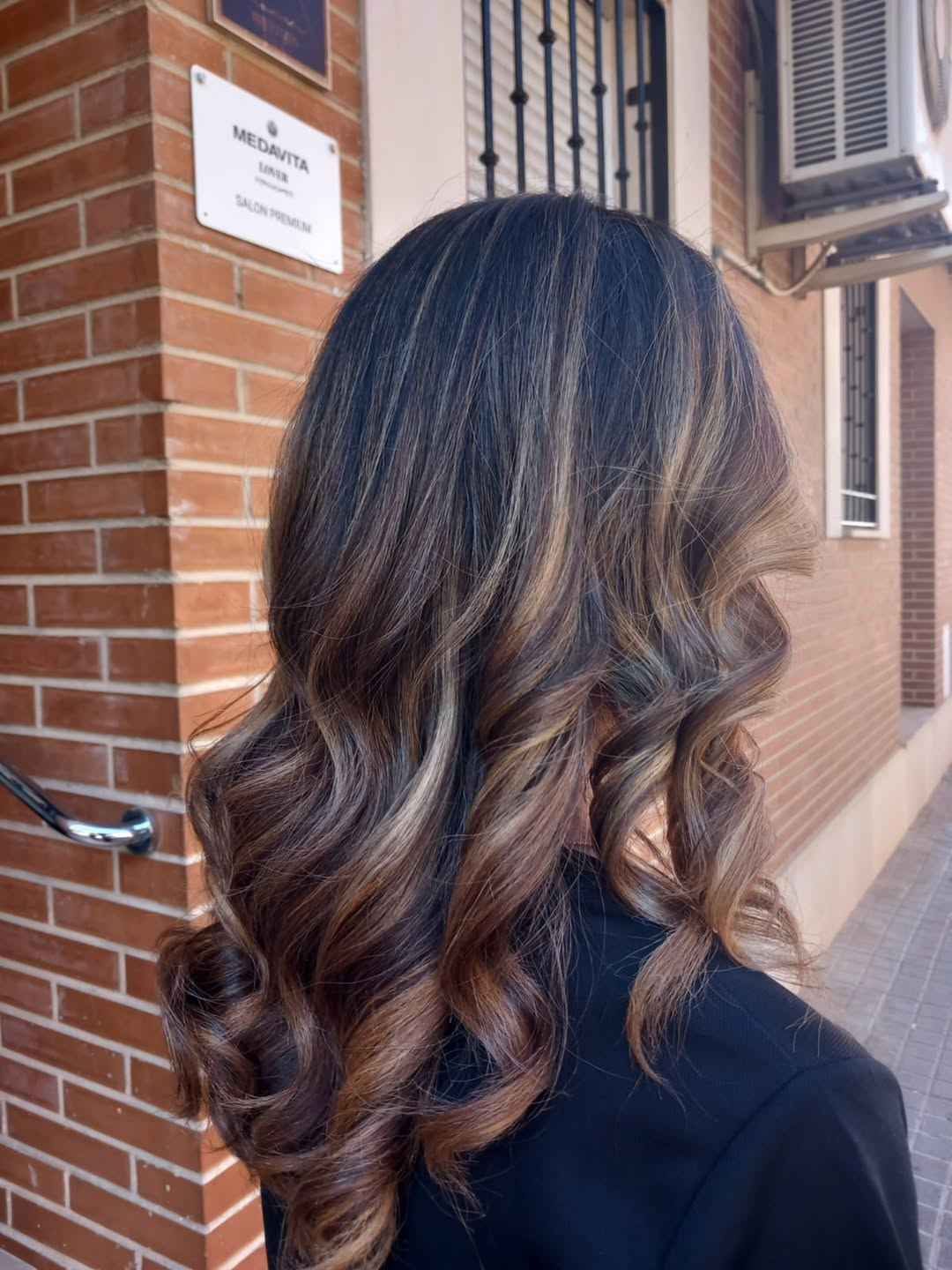 Mujer con cabello castaño ondulado y con reflejos.