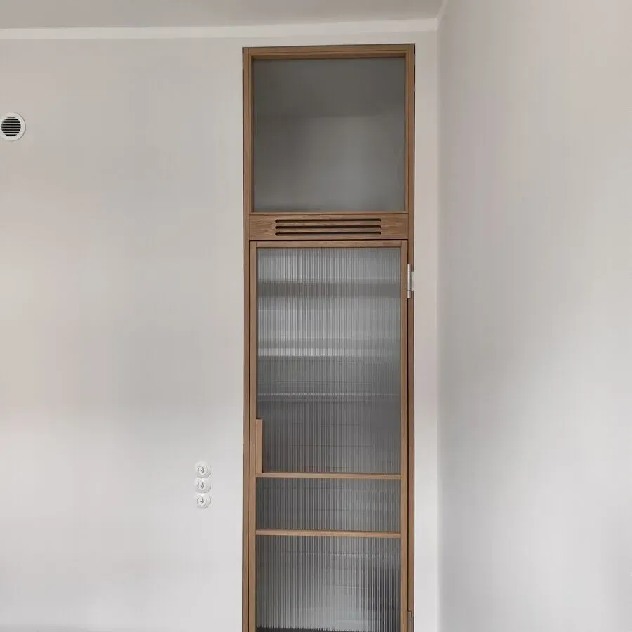 Hoher, eingebauter Holzschrank mit Milchglastüren und oberem Fenster, eingefasst in weiße Wände.