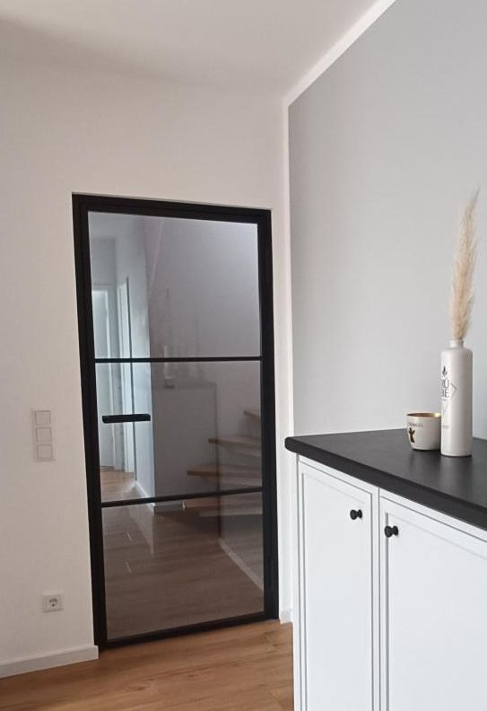 Schwarze Glastür, weiße Wände, dunkler Schrank mit Dekoration. Innenansicht, Flur.