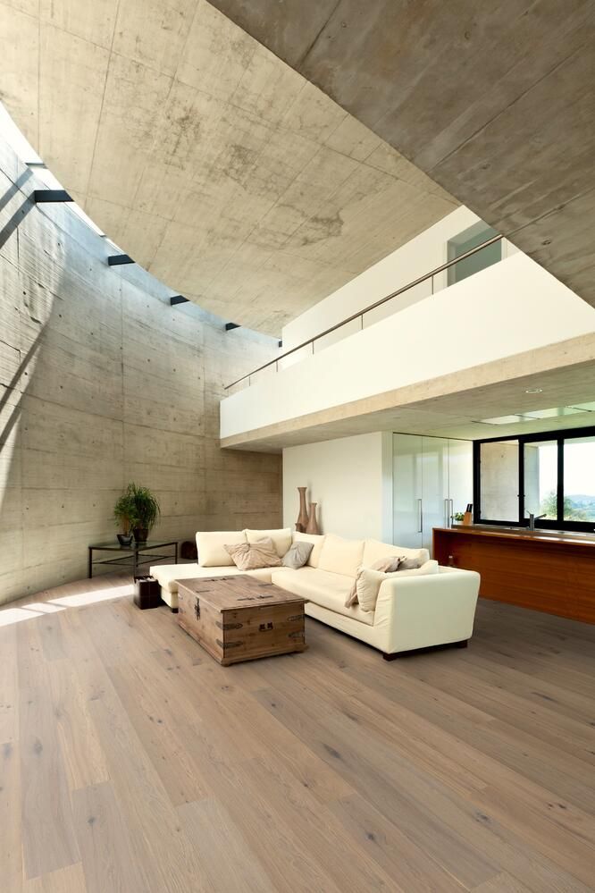 Modernes Wohnzimmer mit hellen Holzböden, einem weißen Sofa und einer Betondecke.