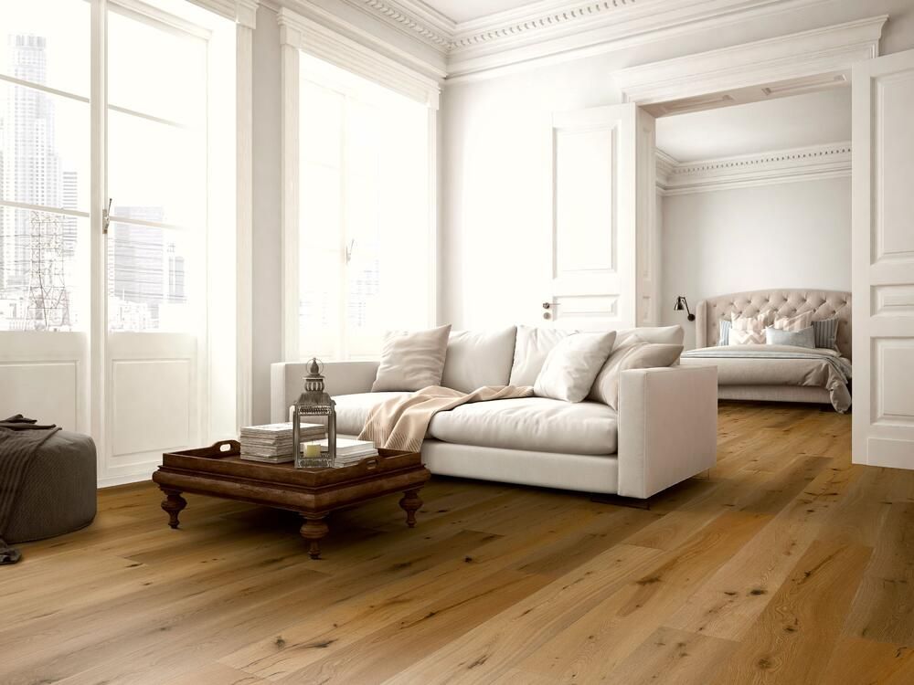 Wohnzimmer mit hellem Holzboden, weißen Wänden und einem weißen Sofa, im Hintergrund ist ein Schlafzimmer zu sehen.