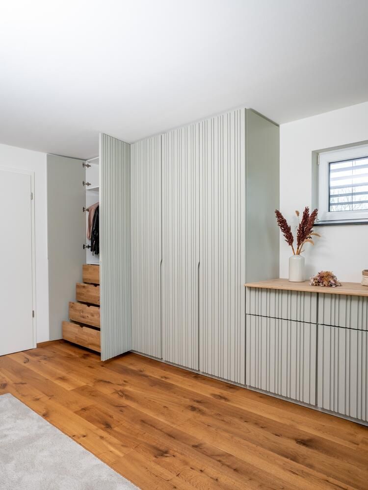 Helles Zimmer mit Holzboden und maßgefertigten, vertikal gefütterten Schranktüren; eine Treppe mit Schubladen führt zu zusätzlichem Stauraum.