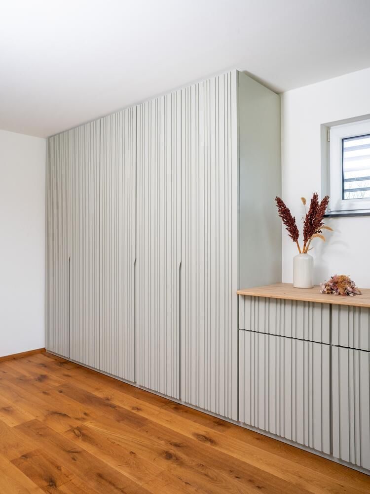 Hohe, hellgraue, gerippte Schranktüren und ein kleiner Seitenschrank mit hölzerner Arbeitsplatte.