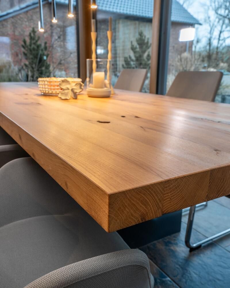 Ein Esstisch aus Holz mit modernen Stühlen, Kerzen und Dekoration steht neben einem Fenster.