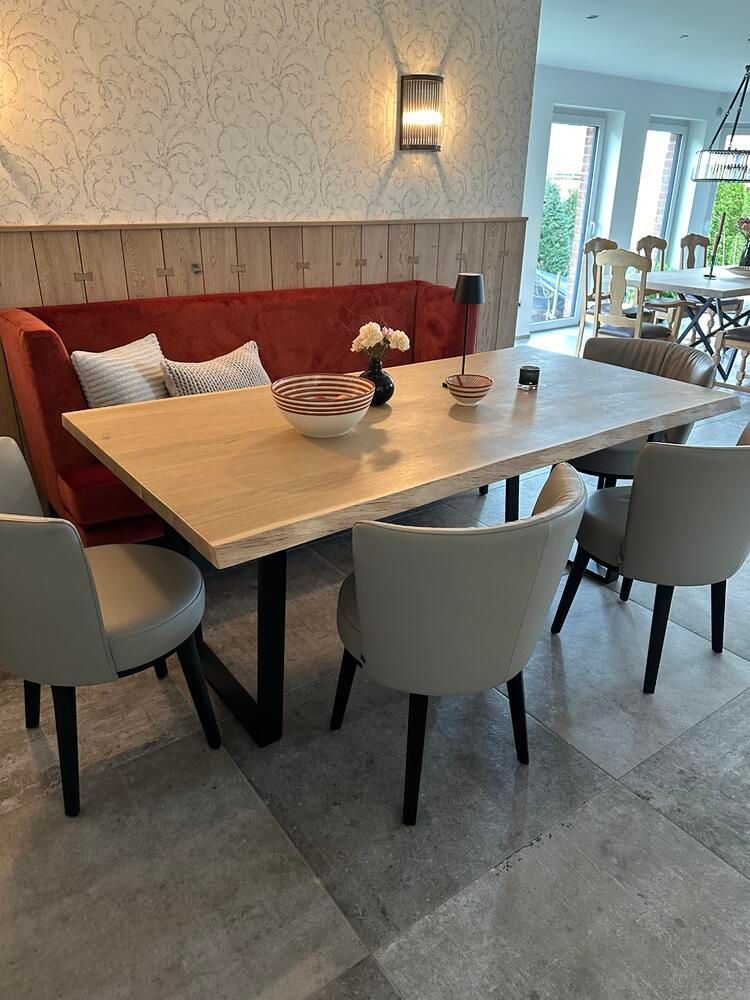 Essbereich mit einer roten Sitzecke, einem Holztisch und grauen Stühlen auf gefliestem Boden.