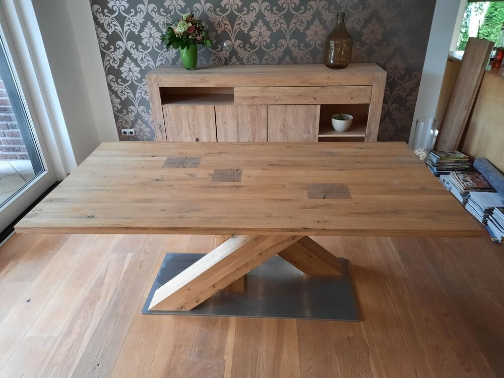 Holzesstisch mit einzigartigem Gestell, hölzernes Sideboard und Blumenarrangement an tapezierter Wand.