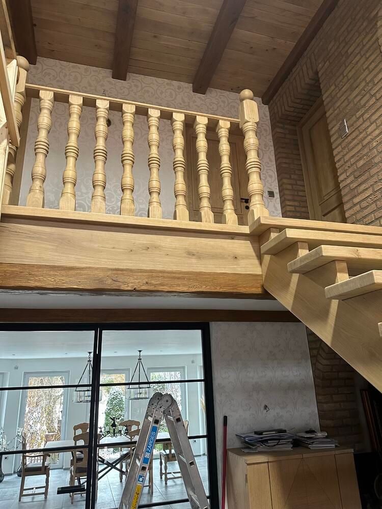 Holzgeländer und Treppe in einem Haus. Darunter ist das Esszimmer mit Glastüren zu sehen.