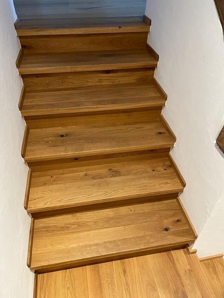 Holztreppe mit sechs Stufen vor weißen Wänden.