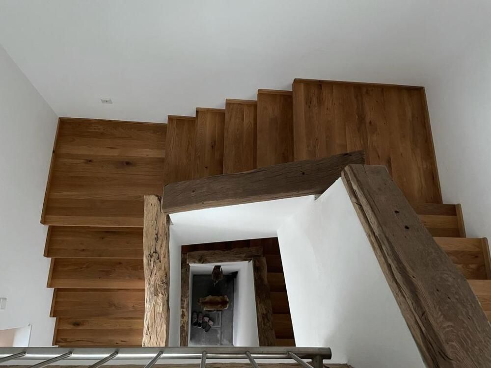 Holztreppe mit natürlicher Oberfläche, von oben betrachtet, die in einen Türbereich hinabführt.